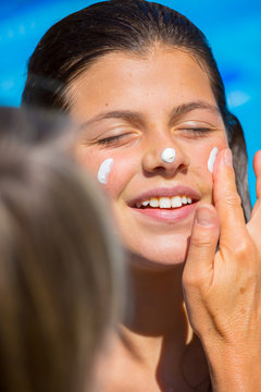 A mother applying a protect sun cream on the face of her smiling young girl