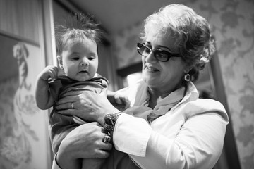 Baby boy in grandma's hands. Woman holding the baby and smiles