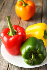 Four fresh pepper on plate on grey wooden background