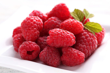 Red raspberries on plate on white wooden background