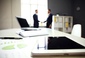 Close-shot of a tablet computer with businessmen handshaking 