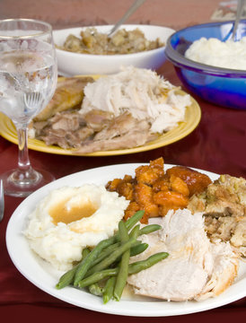Turkey Dinner on the Table – A Thanksgiving meal with a plate of turkey, stuffing, candied yams, and mashed potatoes with gravy. Other food in the background.