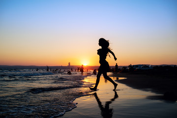 Woman at the beach running by the sea at sunset