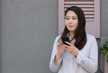 Young Asian woman in city texting cell phone