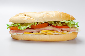 Sandwich on a white plate with turkey breast, tomato and lettuce.