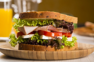 Sandwich on a white plate with turkey breast, tomato and lettuce.