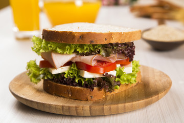 Sandwich on a white plate with turkey breast, tomato and lettuce.