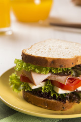 Sandwich on a white plate with turkey breast, tomato and lettuce.