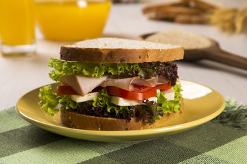 Sandwich on a white plate with turkey breast, tomato and lettuce.