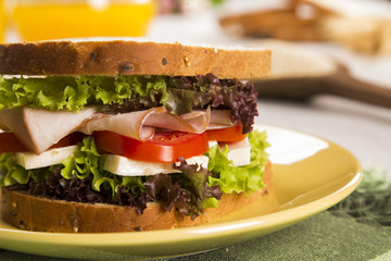 Sandwich on a white plate with turkey breast, tomato and lettuce.