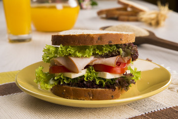 Sandwich on a white plate with turkey breast, tomato and lettuce.