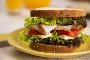 Sandwich on a white plate with turkey breast, tomato and lettuce.