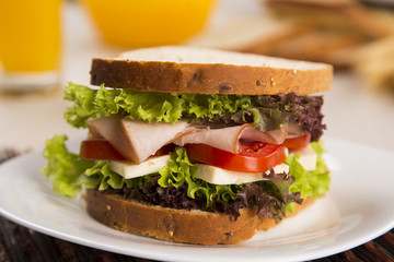 Sandwich on a white plate with turkey breast, tomato and lettuce.