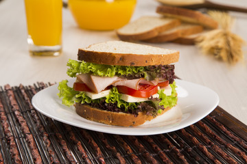 Sandwich on a white plate with turkey breast, tomato and lettuce.