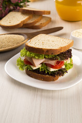 Sandwich on a white plate with turkey breast, tomato and lettuce.