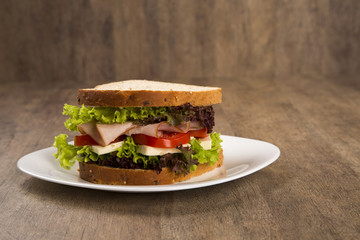 Sandwich on a white plate with turkey breast, tomato and lettuce.