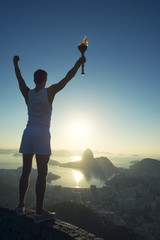 Athlete holding sport torch standing with arms raised in silhouette against Rio de Janeiro Brazil...