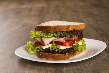 Sandwich on a white plate with turkey breast, tomato and lettuce.