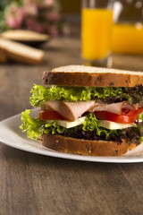 Sandwich on a white plate with turkey breast, tomato and lettuce.
