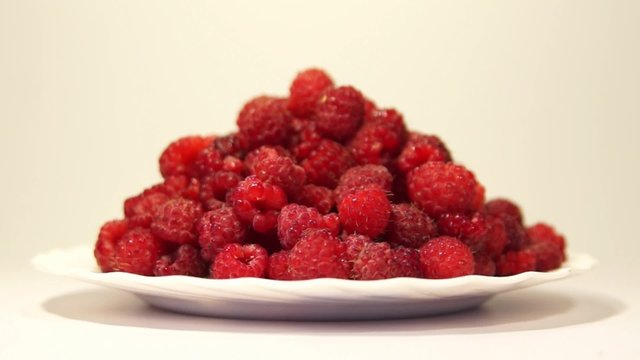 White plate with fresh red raspberries rotating
