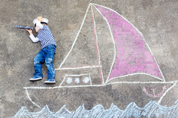 Little boy having fun with ship picture drawing with chalk