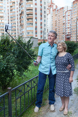 Mature people using selfie stick, man holding monopod with smartphone in hand