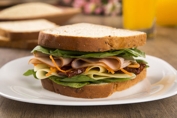 Sandwich on a white plate with turkey breast, tomato and lettuce.