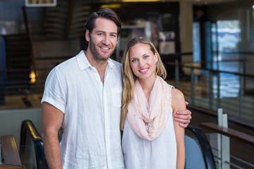 Smiling couple putting arms around in front of escalator