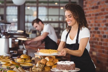 Smiling waitress holding cake in front of colleague