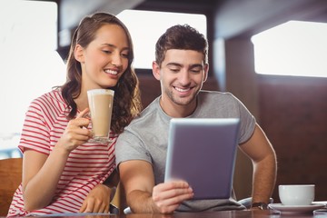 Smiling friends drinking coffee and looking at tablet computer