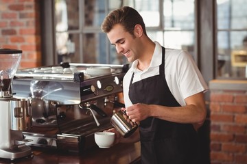 Smiling barista pouring milk into cup - obrazy, fototapety, plakaty