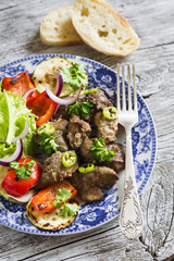 fried chicken liver and grilled vegetables - red pepper, zucchini, green salad on a light wooden background