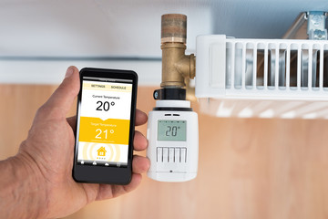 Person Hand Adjusting Temperature Of Thermostat Using Cellphone