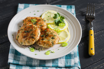 chicken cutlets with lemon and herbs on a white plate on a dark wooden background