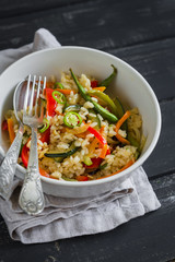 rice with roasted vegetables in an Asian style in a white bowl on a dark wooden background