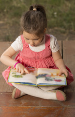Outdoor portrait of an adorable young little girl reading a book in the garden