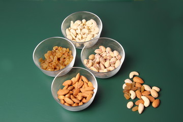 Cashew raisin almond and pistachios in different bowls photographed over green surface