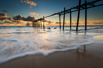 sea waves lash line impact on the sand beach with old wood bridg