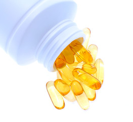 Omega 3 fish oil capsules spilling out of a bottle on a white ba