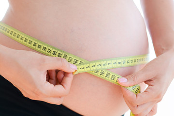 Woman with a pregnancy belly measuring herself with a yellow measuring tape