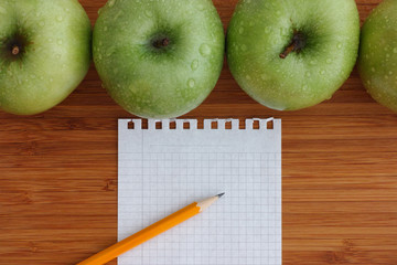 Green apples on a wooden background with sheet of paper and penc