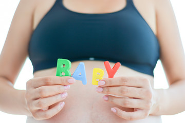 Young expectant mother with letter blocks spelling baby on her pregnant belly