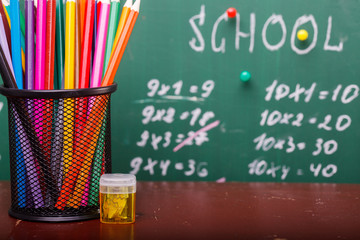 Colorful pencils of red yellow orange violet purple pink green and blue in stationary cup and steel standing on brown school desk on written with white chalk blackboard backgroung on lesson of math