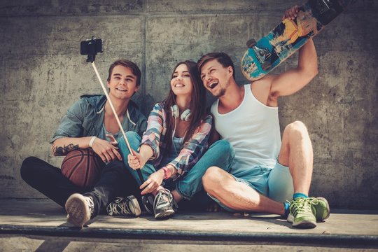Cheerful friends with with skateboard taking selfie outdoors