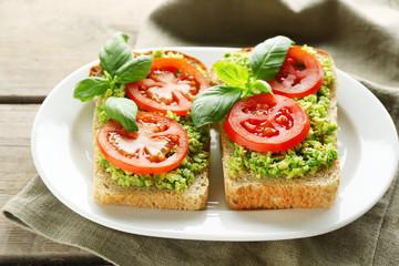 Vegan sandwich with avocado and vegetables on plate, on wooden background
