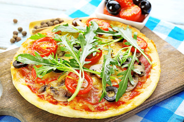 Tasty pizza with vegetables and arugula on cutting board on table close up