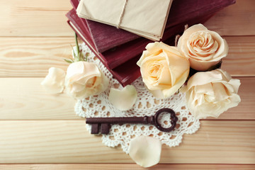 Fresh roses with old book, key and letters on wooden table background. Vintage concept