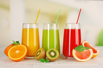 Glasses of different juice with fruits and mint on bright background