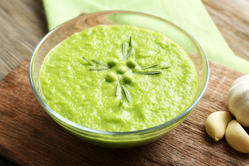 Green pea soup in glass bowl on wooden cutting board, closeup