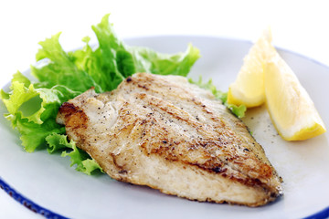 Dish of fish fillet with lettuce and lemon on plate close up